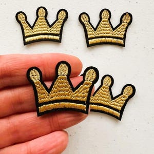 May include: Four gold embroidered crown patches with black outlines. The crowns are approximately 2.5 cm in diameter.