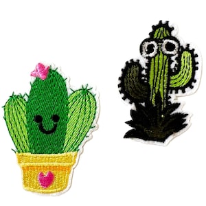 May include: Two embroidered cactus patches. One is green with a pink flower and a smiling face, potted in yellow. The other is green with black accents and large eyes.