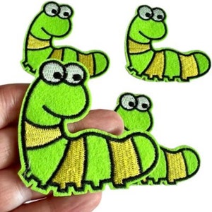 May include: Four green and yellow embroidered iron-on patches of cartoon caterpillars. Each caterpillar has a smiling face with two large eyes.