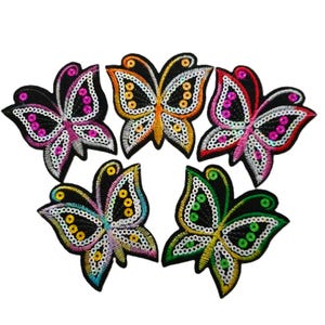 May include: Five colourful butterfly-shaped iron-on patches with sequins. The butterflies are in shades of pink, orange, green, and blue.
