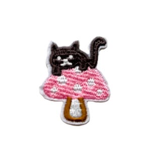 Peut inclure: Un chat noir assis sur un champignon rose à pois blancs. Le champignon a un pied brun.