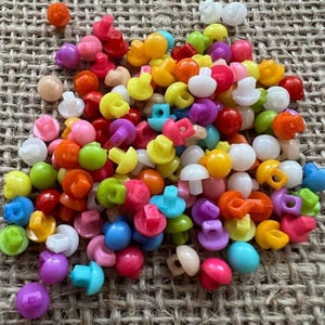 May include: A large pile of colourful plastic buttons in a variety of shapes and sizes. The buttons are mostly round, but some are square or rectangular. The buttons are in a variety of colours, including red, orange, yellow, green, blue, purple, and white.
