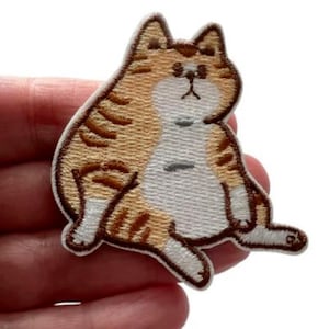 May include: Embroidered patch featuring a cartoon cat in shades of orange, brown, and white. The cat is depicted in a relaxed pose with its legs extended. The patch has a white border and is suitable for clothing or accessories.