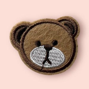 May include: Brown embroidered bear face patch with a white nose and mouth.