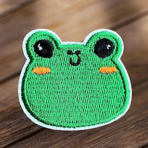 May include: Green embroidered frog patch with white stitching and black eyes. The frog has a small orange smile.
