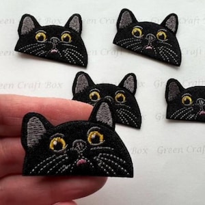 May include: Five black cat face iron-on patches with yellow eyes and gray ears. The patches are embroidered with black thread and have a pink tongue.