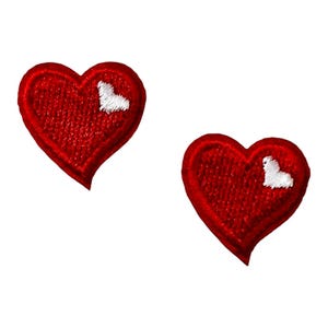 May include: Two heart-shaped embroidered patches featuring a vibrant red thread base with a small, white, stitched highlight detail on the upper right side of each heart, showcasing a textured fabric finish with defined borders.