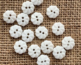 Könnte beinhalten: Eine Sammlung von 14 weißen Plastikknöpfen mit Blumenmuster. Jeder Knopf hat zwei Löcher und ein Spiralmuster.