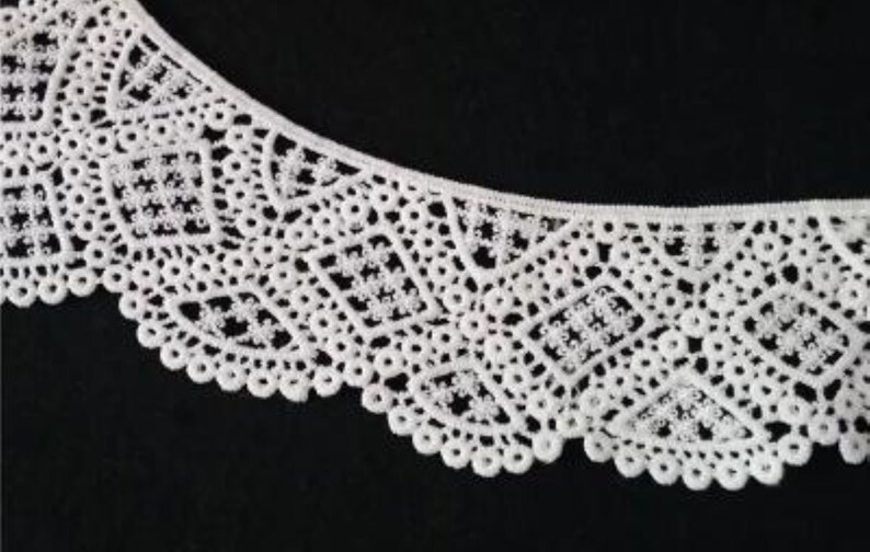 May include: White lace trim with a delicate, intricate pattern. The lace has a scalloped edge and is perfect for adding a touch of elegance to any project.