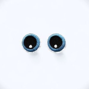 May include: Two blue embroidered googly eyes with white pupils and black centres.