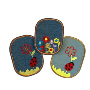 May include: Three denim patches with embroidered flowers and ladybugs. The patches are oval shaped and have a yellow border.