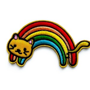 May include: An embroidered iron-on patch featuring a yellow cat head with pink inner ears and black facial features, attached to a multi-colored rainbow arch that extends from the cat's head to a curved tail on the right side, outlined in gold.