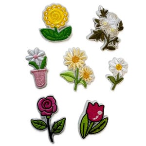 May include: A set of eight embroidered iron-on patches featuring various flower designs. The patches include a yellow sunflower, a white daisy in a pink pot, a white daisy with green leaves, a white flower with green leaves, a yellow and white daisy, a pink rose, a pink tulip, and a white flower with green leaves.