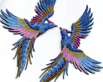 Op de afbeelding: Twee geborduurde strijk-op patches van blauwe, roze en gouden vogels met uitgespreide vleugels.