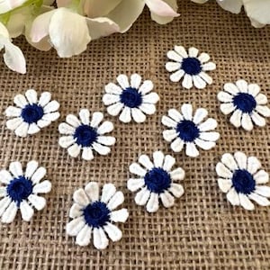 May include: Ten white fabric daisy appliques with navy blue centers. The appliques are arranged on a burlap background.