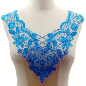 May include: A vibrant blue lace applique, featuring floral and leaf patterns, displayed on a mannequin. The intricate design includes a V-neck shape and delicate openwork, perfect for embellishing garments or crafts.