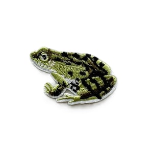 May include: Green and black embroidered frog patch. The frog is sitting on a white background.