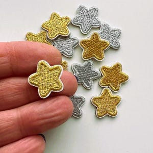 May include: Assortment of gold and silver star-shaped iron-on patches. The patches are approximately 2.5 cm in size and have a white outline.