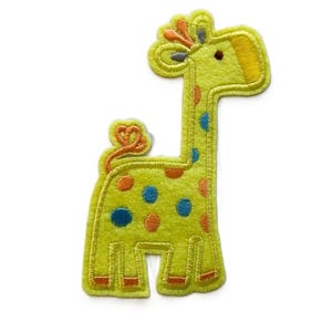 May include: A yellow felt giraffe applique with orange, blue and grey embroidered details. The giraffe has a spotted pattern and a small tail.