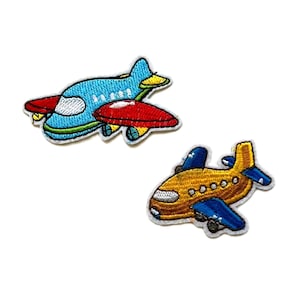 May include: Two embroidered iron-on patches of aeroplanes. One aeroplane is blue with red accents and the other is yellow with blue accents.