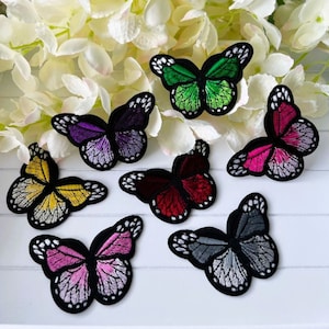 May include: Assortment of colourful embroidered butterfly iron-on patches. The patches feature butterflies in shades of purple, green, red, yellow, pink, and grey.