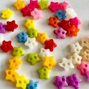 May include: Assortment of colourful plastic star-shaped buttons with two holes each. The buttons are in various colours, including red, orange, yellow, green, blue, purple, and white.
