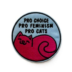 Peut inclure: Un patch brodé bleu et rose à repasser avec un chat endormi et le texte "Pro Choice Pro Feminism Pro Cats".