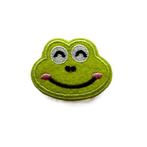 May include: Green felt frog patch with a smiling face, closed eyes, and a pink tongue sticking out.