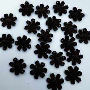 Peut inclure: Plusieurs petites appliques en forme de fleurs, de couleur marron foncé. Chaque applique présente un motif ajouré détaillé avec de multiples pétales. Les appliques sont disposées sur une surface claire, créant un aspect délicat et texturé.