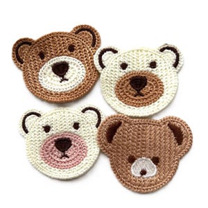 Könnte beinhalten: Vier gehäkelte Bärenkopf-Applikationen. Zwei sind braun mit weißer Nase und Augen, und zwei sind weiß mit brauner Nase und Augen. Ein weißer Bär hat eine rosa Nase.