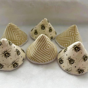 May include: A set of five cone-shaped fabric covers featuring two distinct patterns: a cream-colored textile with a repeating black bee print and a cream-colored textile with a geometric gold chevron and diamond pattern on a white base.