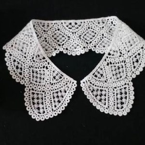 May include: White lace collar with a scalloped edge. The collar is made of delicate, intricate lace with a geometric pattern.