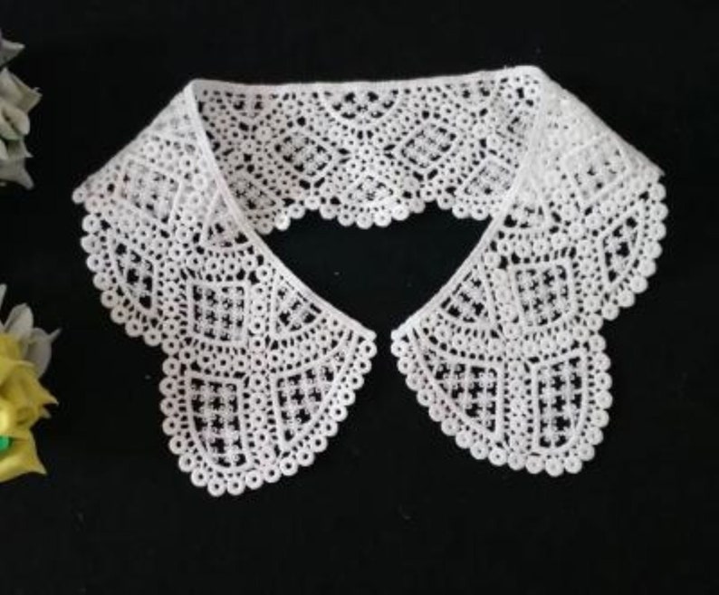 May include: White lace collar with a scalloped edge. The collar is made of delicate, intricate lace with a geometric pattern.