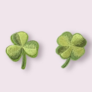 May include: Two green embroidered shamrock patches. The shamrocks are four-leaf clovers with a green stem.