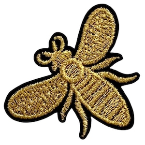 May include: A gold embroidered bee patch with black outlining. The bee is facing right and has a detailed design.