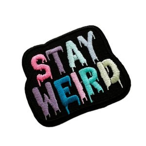 Peut inclure: Un patch thermocollant noir avec les mots "STAY WEIRD" brodés en couleurs arc-en-ciel. Les lettres sont en forme de gouttes, ce qui donne au patch un aspect amusant et original.