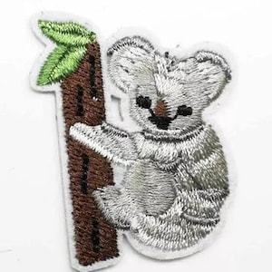 May include: Embroidered iron-on patch of a gray koala bear climbing a brown tree trunk with green leaves.