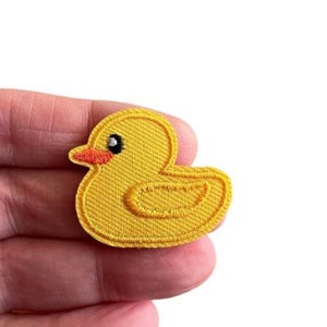 May include: A yellow rubber ducky patch with black eyes and an orange beak. The patch is embroidered with a textured surface.