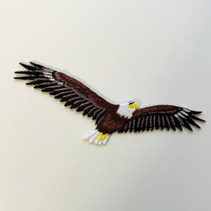 Peut inclure: Patch brodé thermocollant représentant un aigle chauve brun et blanc avec un bec et des serres jaunes, en vol, les ailes déployées.