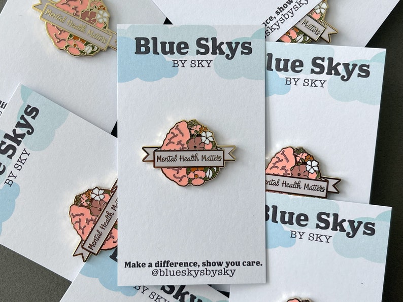 May include: Enamel pin featuring a stylized brain design with floral accents and the text "Mental Health Matters" on a banner. The pin is displayed on a white card with the "Blue Skys by Sky" logo and a call to action.