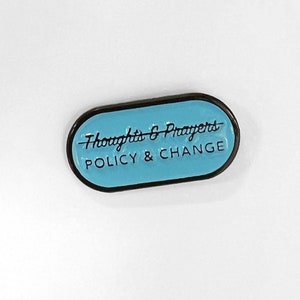 May include: A blue enamel pin with a black border. The pin says "Thoughts & Prayers" with a line through it and "POLICY & CHANGE" below.