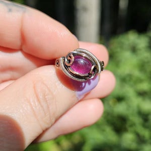 May include: A silver and copper wire wrapped ring with a pink oval gemstone.