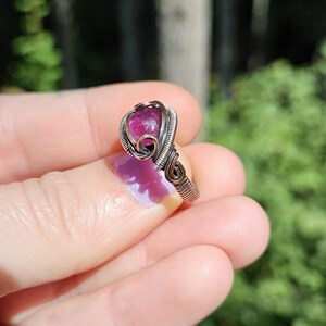 May include: A pink gemstone ring with a wire-wrapped setting. The ring is made of silver wire and has a delicate, intricate design.
