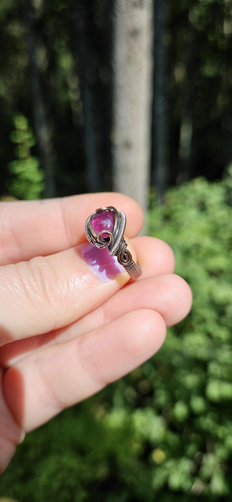 May include: A pink gemstone ring with a wire-wrapped setting. The ring is made of silver wire and has a delicate, intricate design.