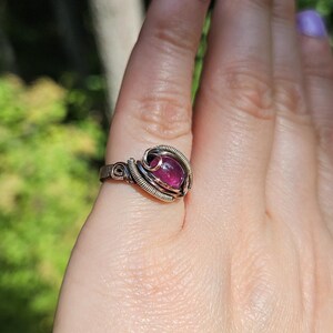 May include: A silver wire wrapped ring with a pink gemstone. The ring is on a person's finger.