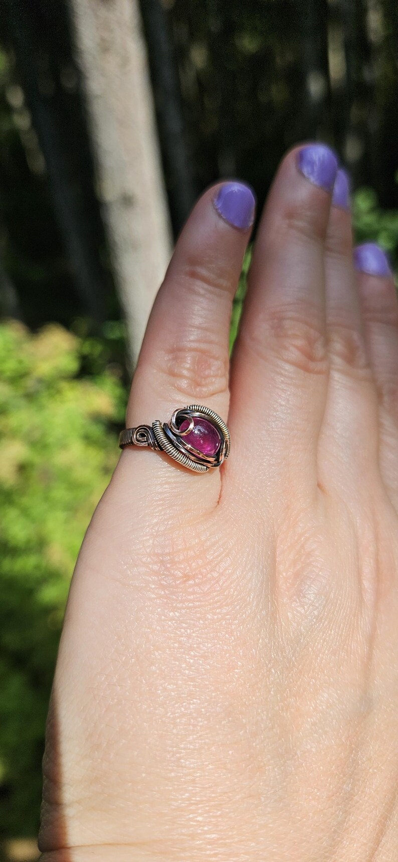 May include: A silver wire wrapped ring with a pink gemstone. The ring is on a person's finger.