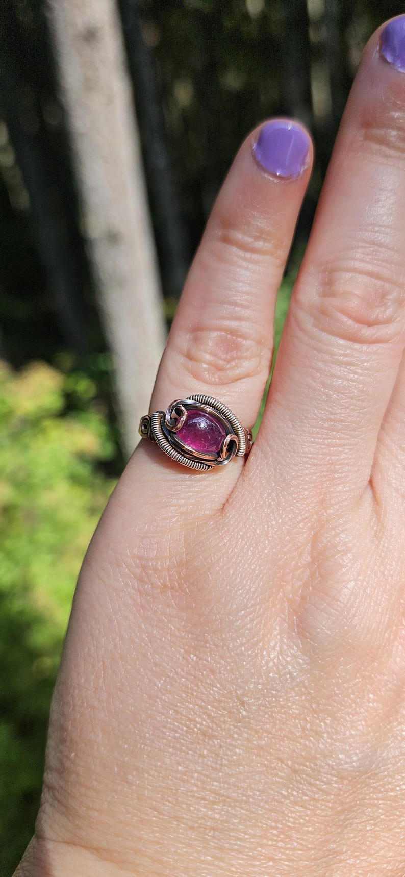 May include: A copper wire wrapped ring with a purple gemstone. The ring is on a person's finger.