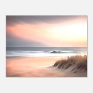 Puede incluir: Una serena escena de playa con un efecto borroso. La imagen presenta una playa arenosa, olas del océano y un cielo con suaves tonos rosados y anaranjados. Una duna con hierba alta es visible a la derecha.