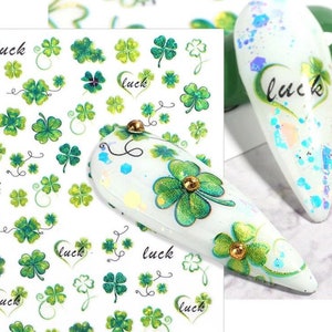 May include: A sheet of nail art stickers with a white background and green four-leaf clovers. The stickers also feature the word "luck" written in cursive.