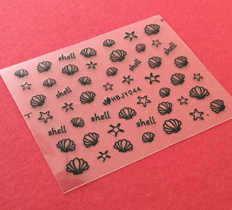 May include: A sheet of clear nail decals with black outlines of seashells and starfish. The sheet has the text "HBJY044" and "shell" repeated multiple times.